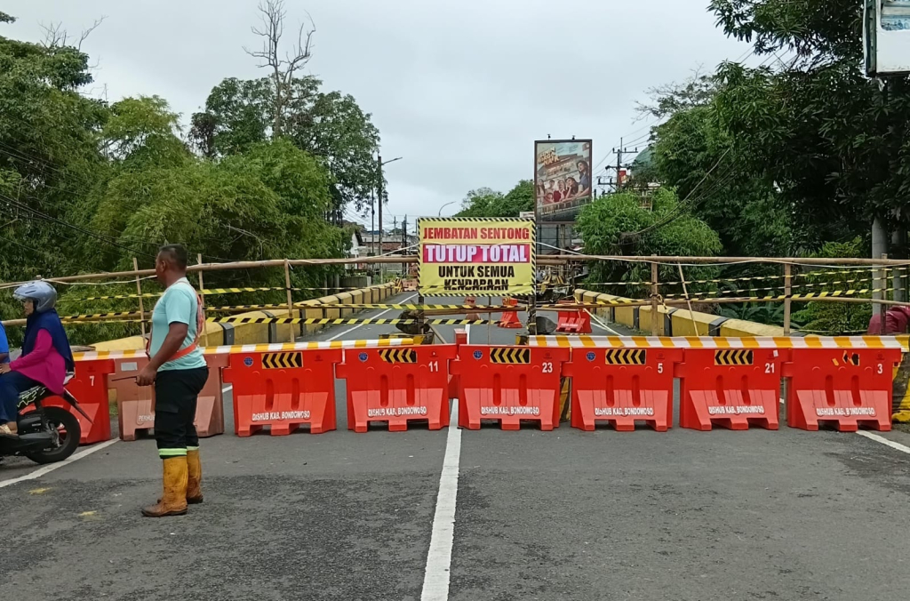Sisi barat Jembatan Sentong di Nangkaan, Bondowoso, ditutup total setelah ambrol akibat hujan deras Senin (23/02/2026). Penutupan jembatan berdampak pada aktivitas perdagangan, distribusi logistik, dan akses warga.