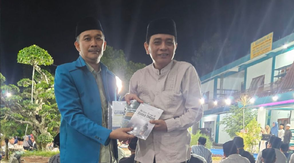 Direktur Utama IBS PKMKK Prof. Dr. KH. Achmad Muhlis (kiri) mempersembahkan buku untuk Kades Lancar H. Mohammad Hosli.